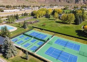Un complesso di campi da tennis con più campi, un'area di parcheggio e vegetazione circostante.