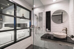 Een moderne badkamer met een douchecabine van glas, een ronde spiegel en een witte wastafel met een zwart aanrecht.