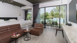 A modern hotel room with a large bed, a sofa, a small table with books, and a balcony with a view of palm trees. - Kokotel Khao Lak Lighthouse (Takua Pa)