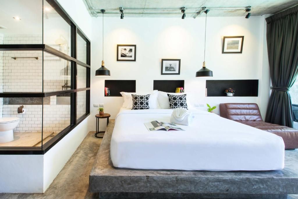 A modern hotel room with a large bed, bedside tables, a glass shower enclosure, and a view of the city.