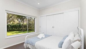 A bedroom with a bed, a window with a view of greenery, and a white wardrobe.