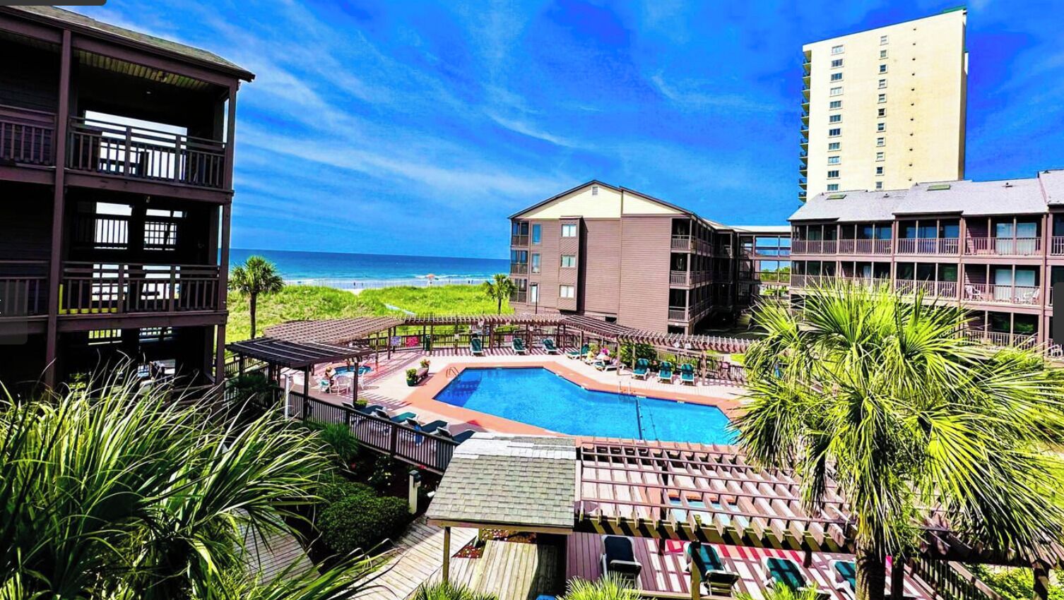 A pool area with a view of the beach, surrounded by buildings.