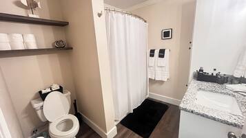A bathroom with a toilet, shower curtain, towel rack, and a sink with a marble countertop.