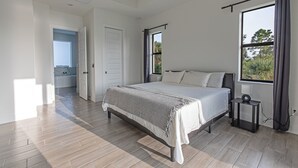 Een moderne slaapkamer met een groot bed, een klein nachtkastje, een raam met gordijnen en uitzicht op de omgeving.