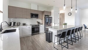 Een moderne keuken met witte kasten, roestvrijstalen apparatuur en een centraal kookeiland met barkrukken.