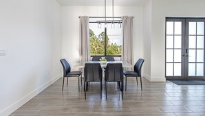 Een eetgedeelte met een tafel, stoelen, een raam met gordijnen en een deur met een deurmat.