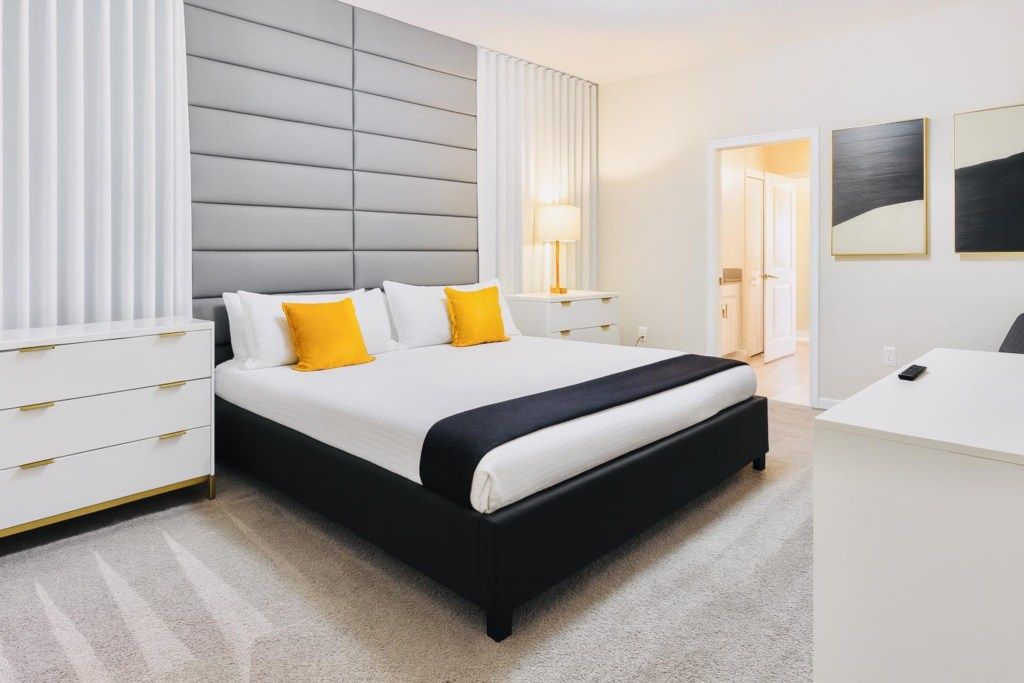 Master bedroom with a king bed, gray padded headboard, white dresser, bedside tables and a plush carpet.