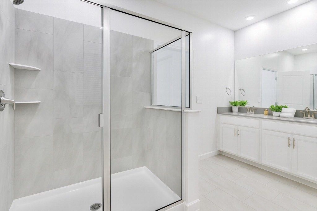 A modern bathroom with a glass-enclosed shower, white cabinetry, and a large mirror.