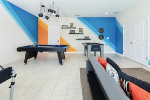 A room with two pool tables, a sofa with patterned cushions, and a wall with sports-themed decorations.