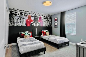 A bedroom with two beds, a Star Wars-themed wall, and a window with blinds.