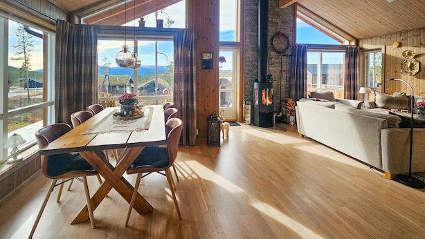 A spacious living area with a large wooden dining table, a fireplace, and a sofa. - 3 bedroom awesome home in Flå (Flå)