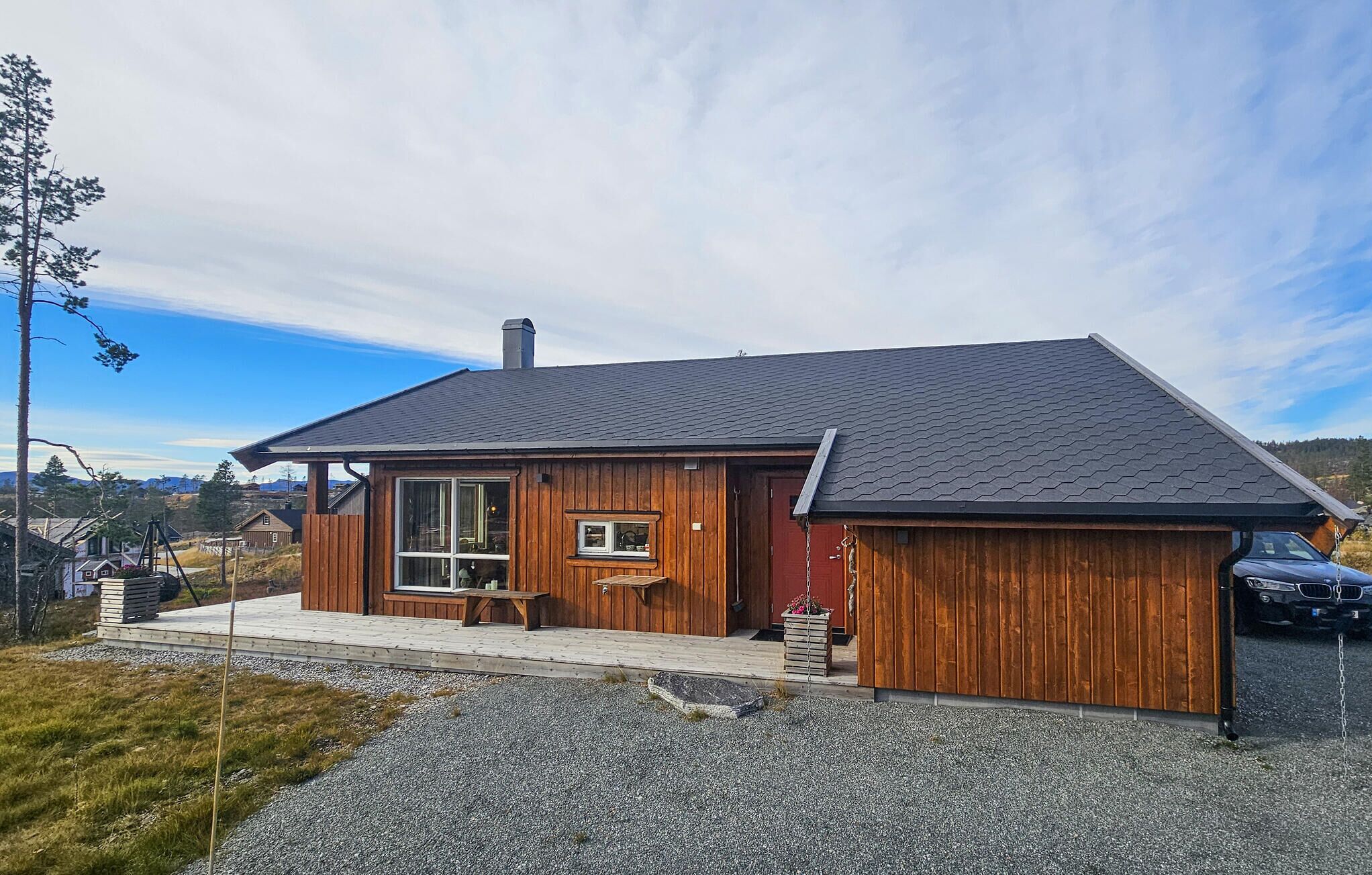 A wooden cabin with a large window, a chimney, and a gravel driveway.