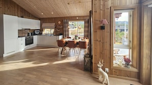 A spacious kitchen with white cabinets, a dining area with a wooden table and chairs, and a large window offering a view of the outdoors. - 3 bedroom awesome home in Flå (Flå)