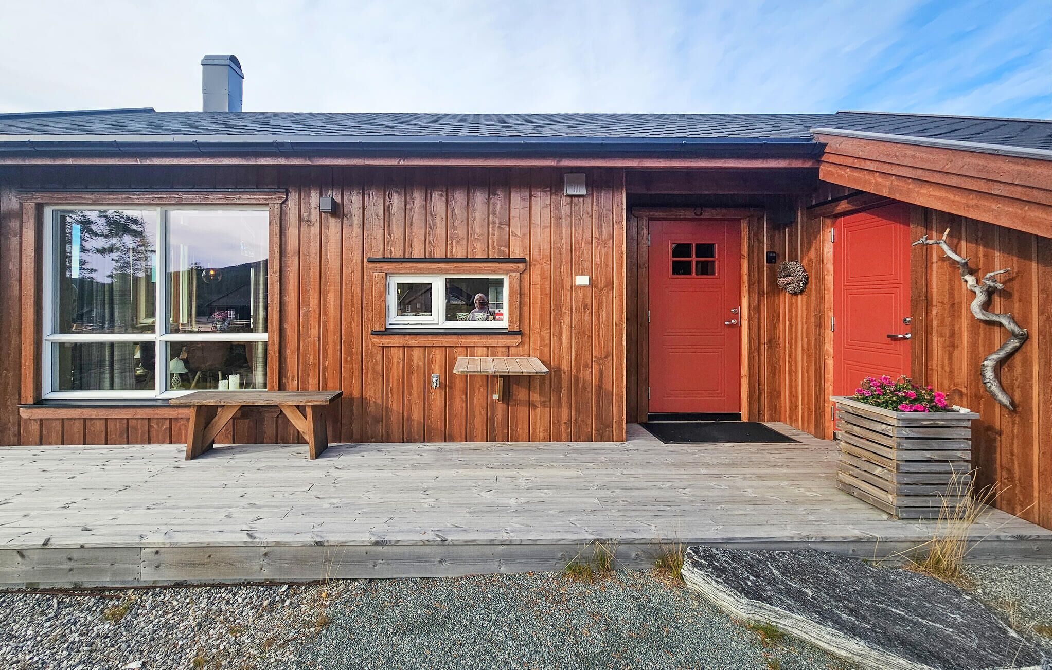 A wooden building with a large window, a small window, a red door, and a bench outside.