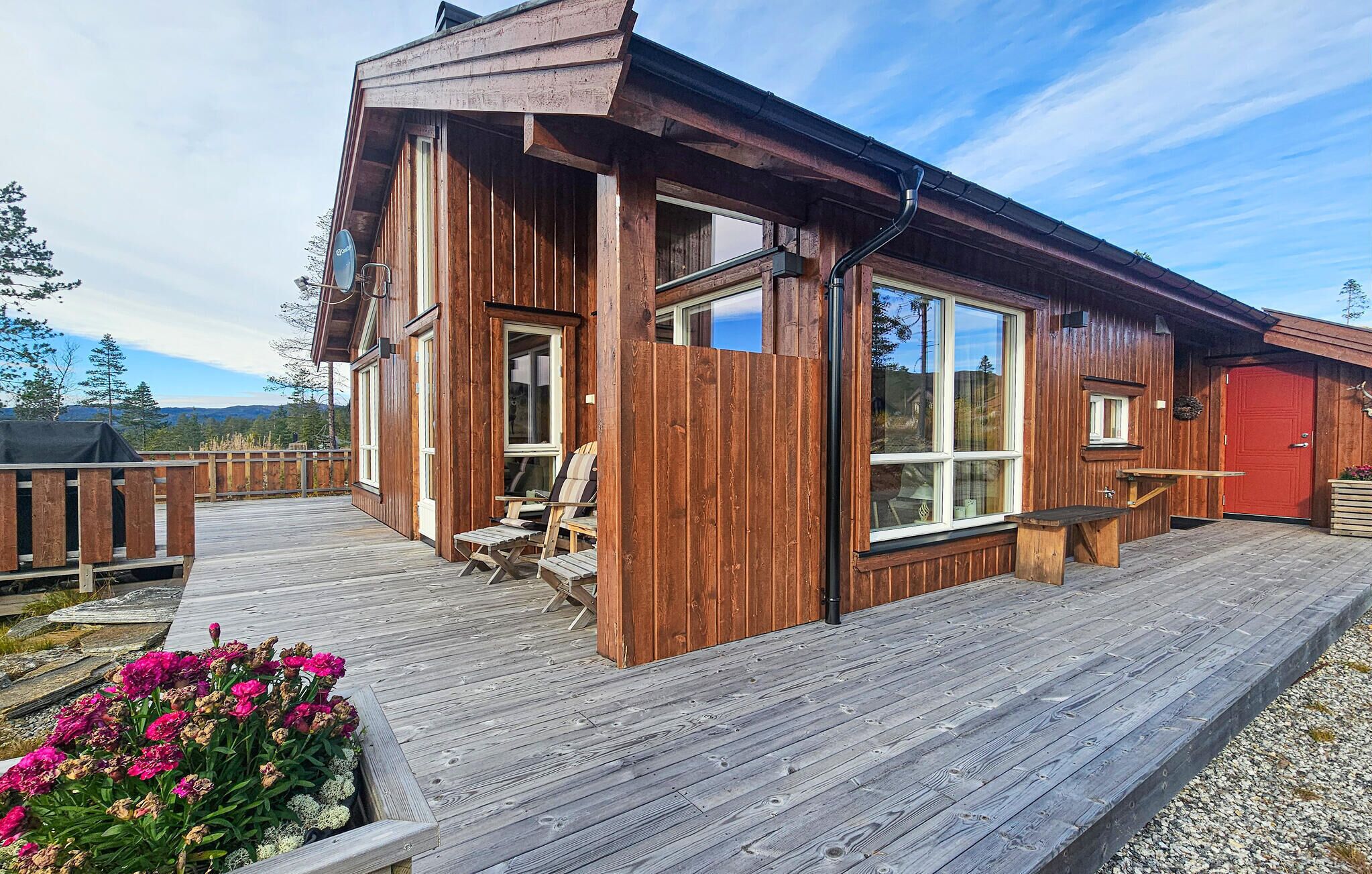 A wooden cabin with a deck, large windows, and a red door.