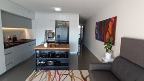 A modern kitchen with built-in appliances, a dining area with a wooden table, and a gray sofa. - Modern 1 bedder with river views in West End (West End)