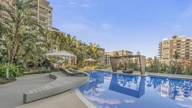 A swimming pool with lounge chairs, surrounded by tropical plants and modern buildings. - Modern 1 bedder with river views in West End (West End)