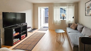 Un salon avec un téléviseur, un canapé et une petite table. Une porte donne sur un balcon.
