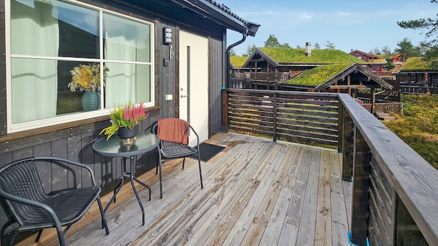 Une terrasse en bois avec une table et des chaises en verre, une plante en pot et une vue sur des maisons traditionnelles aux toits verts.