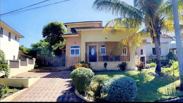 A two-story house with a front yard, a palm tree, and a small garden.