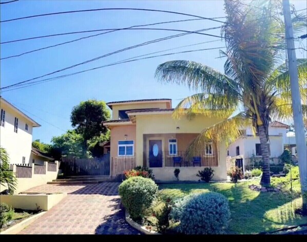 Una casa de dos pisos con un jardín delantero, una palmera y un pequeño huerto.