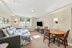 A living room with a sofa, a dining table with chairs, a flat-screen TV, and a window with a view of greenery. - Cozy studio in prime Minneapolis Linden Hills location. (Minneapolis)