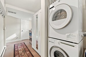A laundry room with stacked washing machines and dryers, a door leading to another room, and a patterned rug on the floor.