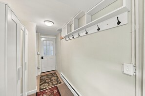 A hallway with a white door, a coat rack, and a patterned rug.
