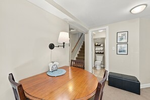 A dining area with a wooden table, chairs, a wall-mounted lamp, and a view into a hallway with a staircase. - Cozy studio in prime Minneapolis Linden Hills location. (Minneapolis)