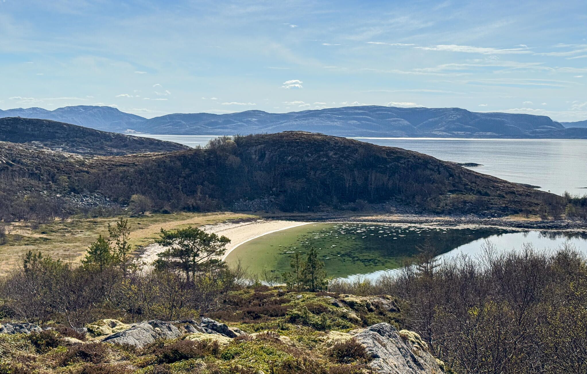 Un paisaje costero con una playa, un lago y montañas a lo lejos.
