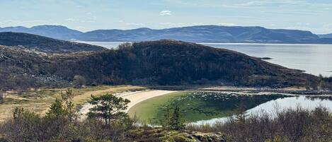 Un paisaje costero con una playa, un lago y montañas a lo lejos.
