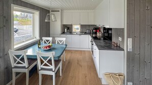 A modern kitchen with white cabinets, a blue dining table, and a view of a driveway. - 4 bedroom awesome home in Færvik (Færvik)