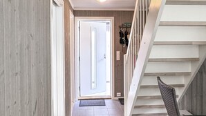 A hallway with a wooden door leading to a bright room, a staircase with a woven handrail, and a wall-mounted coat rack. - 4 bedroom awesome home in Færvik (Færvik)