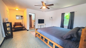 A bedroom with a bed, a ceiling fan, a television, and a window with curtains.