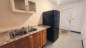 A kitchen with a double sink, wooden cabinets, a black refrigerator, and a white door. - Motel Room 4 with Bar & Grill and Laundromat (Copperhill)