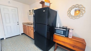 A compact kitchen with a black refrigerator, a microwave, and a wooden bench.