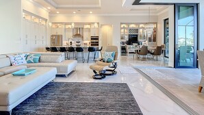 Un salon moderne avec un canapé, des fauteuils et une table basse. Il y a également un coin cuisine avec une table à manger et des chaises. La pièce est dotée d'une grande fenêtre qui offre une vue sur l'extérieur.