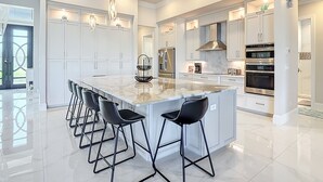 Une cuisine moderne dotée d’un grand îlot central, de tabourets de bar, d’appareils électroménagers en acier inoxydable et de luminaires suspendus.
