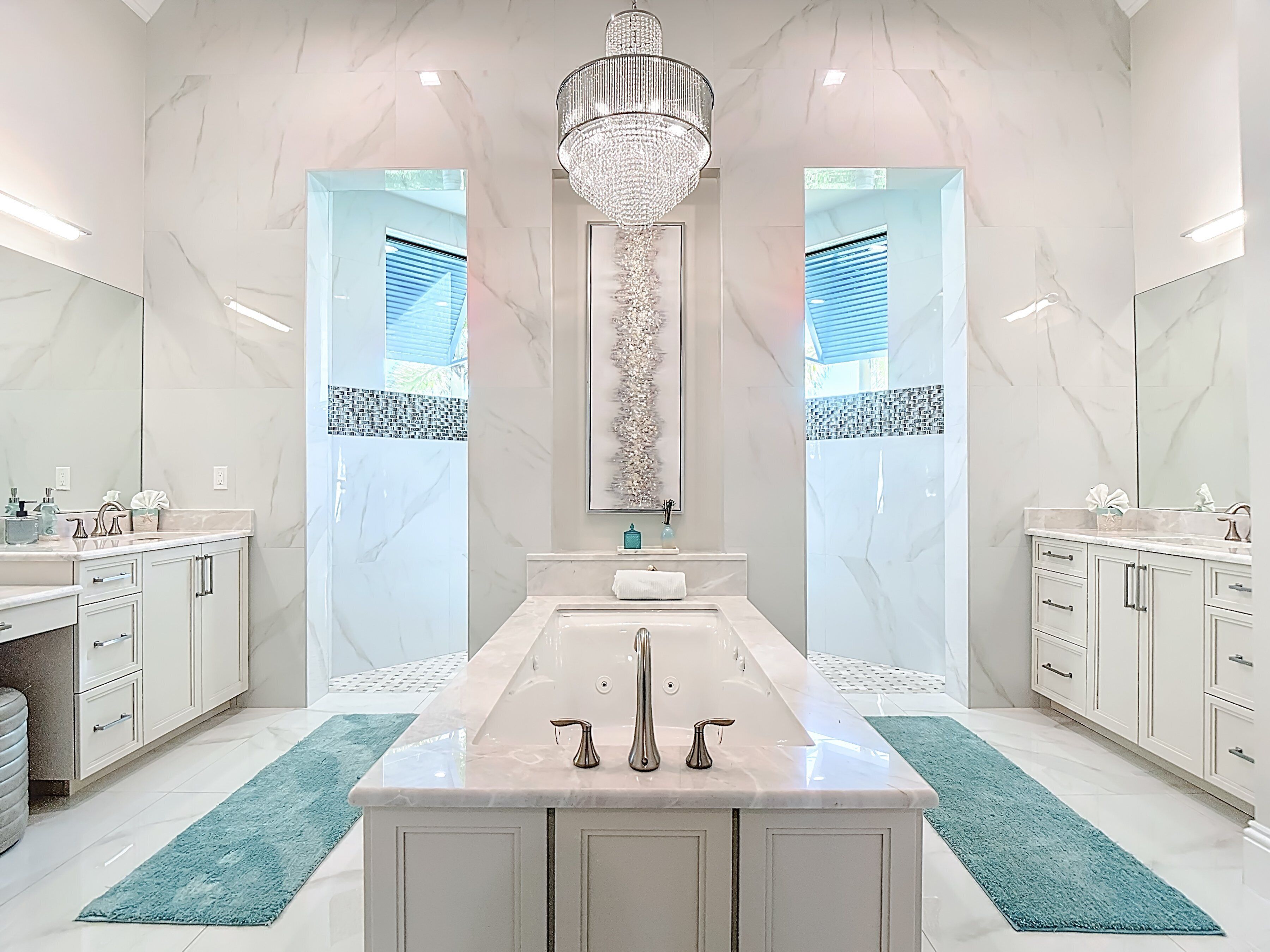 Een moderne badkamer met een centraal geplaatst wastafelmeubel, twee spiegelende wastafels, een kroonluchter en een decoratief wandobject.