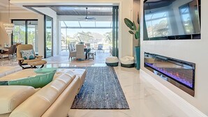 Un salon spacieux doté d’un grand téléviseur, de sièges confortables et donnant sur une terrasse extérieure.