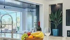 Une cuisine moderne avec une grande fenêtre, un panier de fruits, une bouteille de vin et un verre à vin posés sur le comptoir.