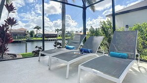 Uma área externa coberta com cadeiras de descanso e vista para um corpo d'água e edifícios ao fundo.
