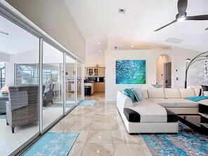 A modern living room with a sofa, a dining area, and a kitchen in the background. - Gulf Access, Heated Pool, Paddle Boards: Parkside (Cape Coral)