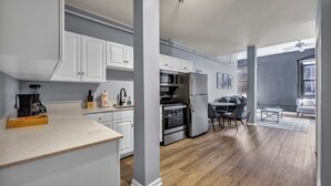 A modern kitchen with white cabinets, stainless steel appliances, and a wooden floor.