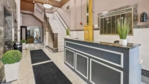 A lobby with a reception desk, a staircase, and a wall-mounted sign.