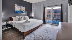 A modern bedroom with a large bed, a desk, and a view of the outside balcony.