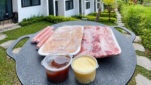 Une table avec de la viande crue, des sauces, et une maison en arrière-plan.