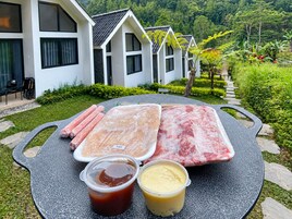 Una mesa con carne cruda, salsas y una casa al fondo.