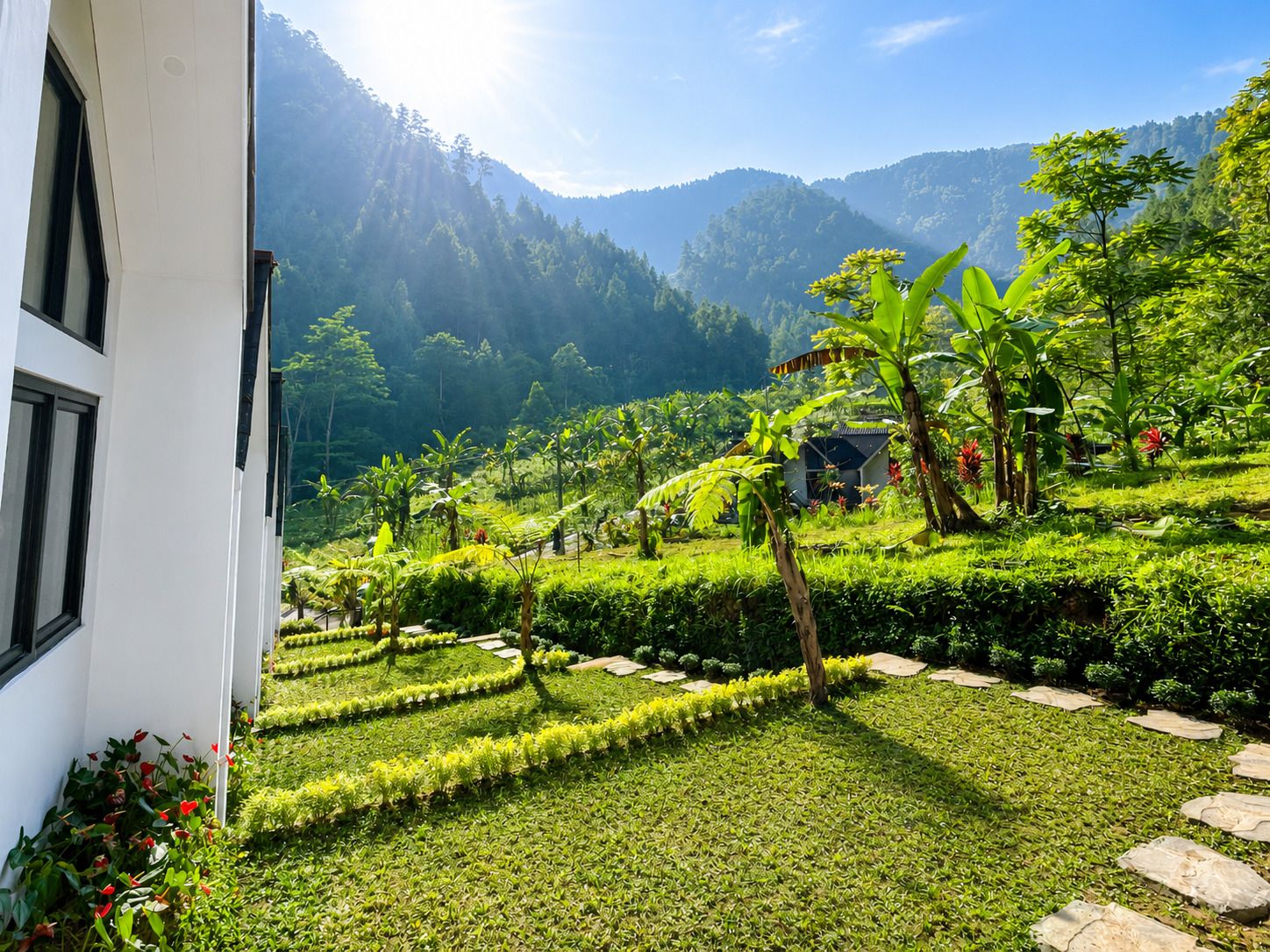 A landscaped garden with a variety of plants and a small structure, surrounded by mountains.