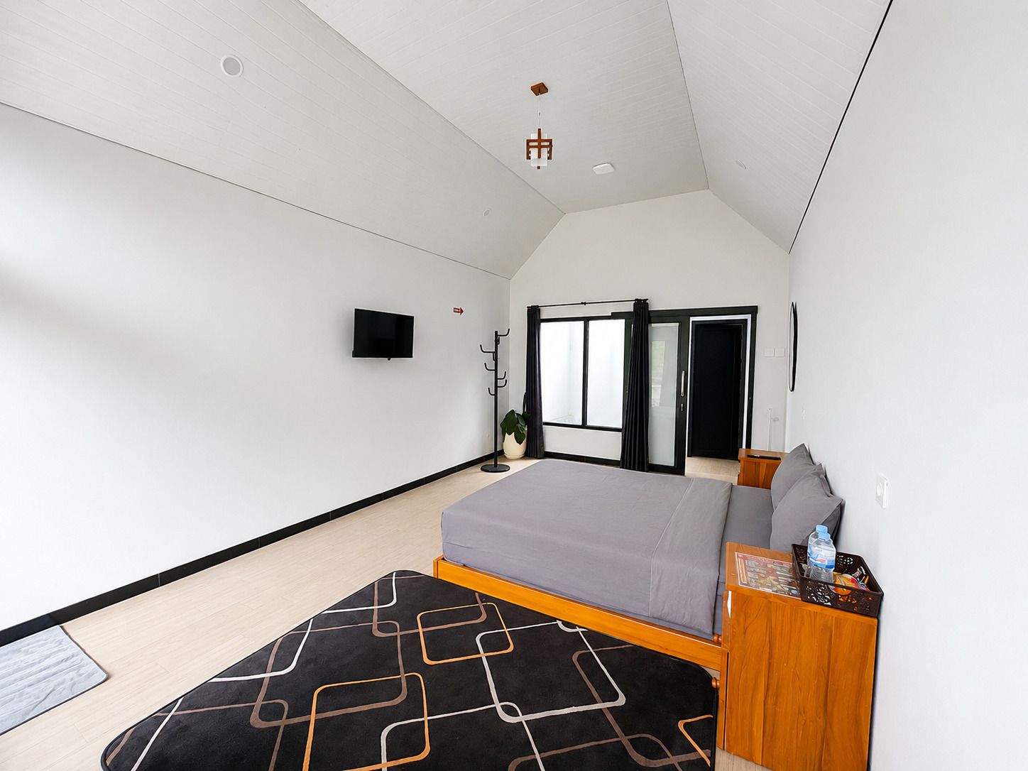 Quarto moderno com cama, televisão, cabideiro e porta deslizante.